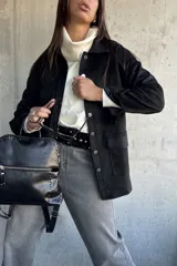 Chaqueta de gamuza negra con cierre frontal de botones metálicos, bolsillos laterales y cuello camisero.