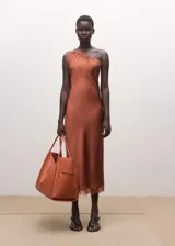 Vestido midi asimétrico de tejido satinado en color tostado, con un tirante fino y otro hombro descubierto. Cuenta con delicados ribetes de encaje a tono en el escote y en el bajo, y una sutil abertura lateral.