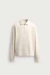Polo de manga larga con diseño relaxed fit, confeccionado en tejido con textura. Cuenta con cuello solapa y cierre frontal de cremallera parcial, y acabados en rib en puños y dobladillo.