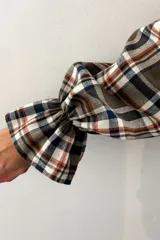 Camisa de manga larga con estampado de cuadros en tonos verde, beige y azul. Presenta cuello clásico, cierre frontal con botones, dos bolsillos delanteros y mangas con puños elásticos y detalle de volado.