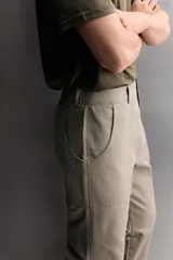 Pantalón de corte tapered fit color beige, confeccionado en tejido ligero de algodón con estructura rip stop. Cuenta con bolsillos de plastrón delanteros con acceso curvado, pinzas en las rodillas para mayor movilidad, y cierre frontal con cremallera y botón a presión.
