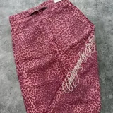 Jean de corte recto y tiro alto con estampado animal print tipo leopardo en tonos rosados y borravino. Cuenta con bolsillos traseros amplios, trabillas para cinturón y una tira ajustable en la parte posterior de la cintura con hebilla metálica. Presenta un bordado lateral con inscripción en cursiva.