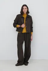 Chaqueta de corte recto y estructura rígida, color marrón oscuro, con cuello camisero, cierre frontal de botones y costuras a la vista en tono contrastante.