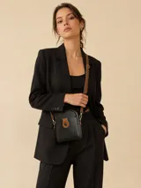 Cartera bandolera de cuero negro con textura granulada, detalle de solapa frontal en color tostado con cierre de botón a presión y correa larga ajustable en color tostado.