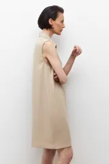 Vestido corto color beige, sin mangas, con cuello camisero, cierre frontal con cordones cruzados y múltiples bolsillos con cierre.