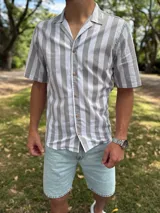 Camisa de manga corta con diseño de rayas verticales en tonos gris y blanco, cuello abierto estilo cubano y cierre frontal con botones de madera.