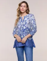 Blusa azul y blanca con estampado floral y geométrico, de calce suelto, con escote redondo, abertura tipo keyhole en el pecho, mangas tres cuartos y ruedo amplio con silueta evasé.