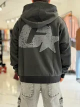 Canguro oversize de color negro, con capucha y bolsillo tipo canguro, confeccionado con un gran estampado gráfico desgastado en la espalda.