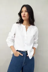Camisa blanca de algodón con cuello mao con leve frunce, abotonadura frontal con botones de nácar y mangas amplias con puños fruncidos.