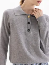 Sweater de punto gris con cuello polo y cierre frontal de tres botones, de manga larga y corte recto.