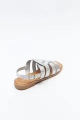 Sandalias plateadas de cuero sintético con tiras anchas cruzadas y detalle central calado. Cierre con hebilla ajustable y suela plana color suela.