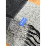 Bufanda rectangular de tejido grueso con diseño de cuadros en tonos azul, naranja, gris y beige, terminada con flecos en los extremos.