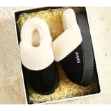 Pantuflas de gamuza negra con plataforma, forradas internamente con corderito sintético color crema. Presentan un diseño sin talón y detalle bordado en el empeine.