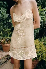 Vestido corto semitransparente de organza con escote en pico y tirantes finos. Presenta aplicaciones de bordados florales a contraste y detalles de cintas horizontales.