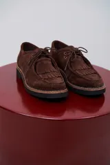 Zapato abotinado de gamuza color caramelo, con cordones, detalle de flecos en el empeine y suela de goma negra con costuras a la vista.