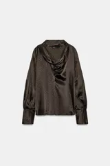 Blusa de seda color marrón oscuro con estampado geométrico sutil. Presenta un diseño de cuello fluido tipo pañuelo, manga larga con puños anchos y una caída suave y elegante.