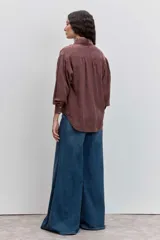 Camisa de satén color azul grisáceo, con cuello mao con detalle de volados, cierre frontal con botones y mangas largas con puños abotonados.