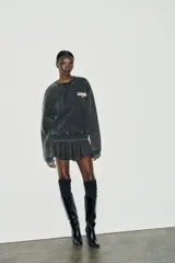 Sudadera de cuello redondo y manga larga, color gris oscuro con efecto lavado. Presenta aplicación de tachas metálicas alrededor del cuello y estampado frontal con el texto "CALIFORNIA USA" en blanco.