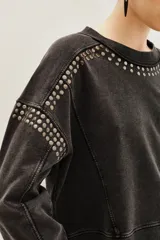 Buzo de algodón color negro con efecto lavado, corte holgado y detalles de tachas metálicas plateadas alrededor del cuello redondo y en los hombros.