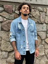 Campera de jean celeste con roturas y desgaste, de corte clásico, con cuello camisero, cierre frontal con botones metálicos, bolsillos con solapa abotonada en el pecho y bolsillos laterales.