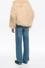Chaquetón corto de corte globo confeccionado en pelo sintético color beige, con cierre frontal de botones de presión, maxi cuello camisero y bolsillos de vivo.