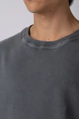 Remeron de corte oversized con cuello redondo y mangas cortas. Presenta un acabado de tela con efecto desgastado y costuras visibles en los bordes, con una etiqueta pequeña en el lateral inferior.