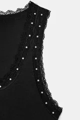 Musculosa de algodón color negro, con escote redondo y tiras anchas. Presenta detalles de encaje negro en los bordes y aplicación de perlas pequeñas alrededor del escote y los hombros.