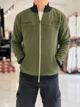 Campera de felpa color verde militar, con cierre frontal completo, bolsillos tipo canguro, cuello alto y detalles en negro en cuello, puños y cintura.