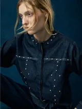 Campera de denim azul oscuro con cuello redondo, cierre frontal con botones metálicos y tachas plateadas en el frente y la espalda.