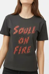 Remera de algodón negra de manga corta y cuello redondo, con estampa frontal que incluye letras rojas y gráficos en tonos dorados.