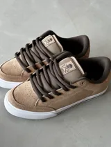 Championes de skate color beige con detalles en marrón, confeccionados en gamuza con puntera de triple costura, lengüeta acolchada con parche de la firma, ojales metálicos y suela vulcanizada blanca.