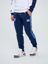 Pantalón de jogging azul marino Umbro del Club Nacional de Football, con cordón ajustable en la cintura, puños elastizados en los tobillos y bandas laterales en tonos de azul. Cuenta con el escudo del club en una pierna y el logo de la marca en la otra.