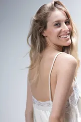 Pijama de satén elastizado color blanco, compuesto por una musculosa de escote en V con tirantes finos y detalles de encaje beige en el escote, y un short a juego con terminación de encaje en las piernas.