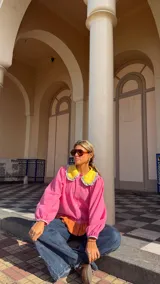 Camisa de manga larga en color rosa, con cuello Peter Pan en color amarillo y detalle de volados en los bordes. Presenta cierre frontal con botones y puños elásticos con detalle de volados.