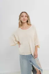 Sweater oversize de tejido liviano color blanco roto, con textura semi traslúcida, escote redondo y mangas amplias estilo murciélago.