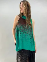 Blusa de satén con escote halter y cuello elevado anudado lateralmente. Presenta un diseño estampado degradado en tonos verde esmeralda y azul, con corte holgado y caída fluida.
