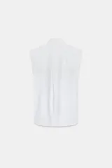 Camisa sin mangas confeccionada en algodón, con cuello redondo y detalle de lazada frontal. Presenta cierre frontal con botones ocultos por solapa y bajo redondeado.