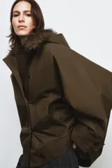 Trench corto de corte recto con capucha y cuello desmontable efecto pelo. Presenta cierre frontal con botones, bolsillos laterales y mangas largas con trabillas en los puños.