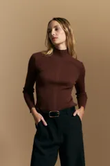 Polera de tejido acanalado color marrón, con cuello alto y mangas largas con terminaciones onduladas en los puños. Presenta un ajuste al cuerpo que estiliza la silueta.
