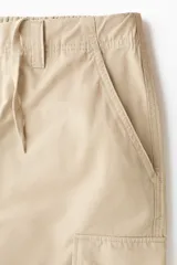Pantalón cargo de lona de algodón con corte relajado, bolsillos laterales con solapa, bolsillos al bies y pliegues reforzados en las rodillas.