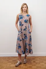 Vestido midi color beige con estampado de hojas en tonos violeta, verde y negro. Diseño sin mangas, con escote redondo y falda acampanada.