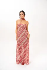 Vestido largo de crochet con escote strapless y lazo integrado para el cuello, con diseño de patrón en zigzag en tonos rojos, blancos y beige, y aberturas laterales en la falda.