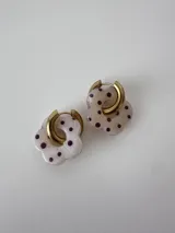 Aros de acero quirúrgico dorado con argolla y dije colgante en forma de flor de resina blanca con lunares violetas.