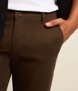 Pantalón de vestir color marrón, de corte slim y largo cropped. Confeccionado en tejido de algodón liso, con bolsillos laterales y traseros. Cierre frontal con botón y cremallera.