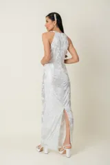 Vestido largo de fiesta en gasa labrada color blanco con detalles plateados, con cuello halter, drapeado en la cintura y tajo en la parte trasera.