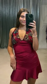 Vestido corto color bordó con escote halter, confeccionado en tela satinada con detalle de apliques de lentejuelas brillantes en el escote y ruedo con volado.