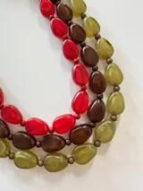 Collar de tres hileras compuesto por cuentas de resina en tonos rojo, marrón y verde oliva, con acabado brillante y translúcido.