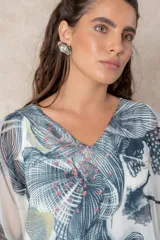 Blusa tipo túnica de gasa semitransparente con escote en V y mangas amplias. Presenta un diseño estampado con efecto acuarela en tonos azules, grises y marrones sobre fondo blanco.