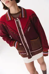 Cardigan de punto con diseño multicolor, cuello tipo polo con rayas, cierre frontal con botones y bolsillos aplicados. Presenta mangas con trama trenzada, coderas en contraste y bordado de la marca en el frente.