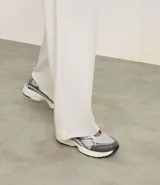 Championes de estilo híbrido entre jogging y Mary Jane, confeccionados en poliuretano. Presentan un diseño con cierre de tira adherente en el empeine, suela robusta y detalles en tonos grises y plateados.